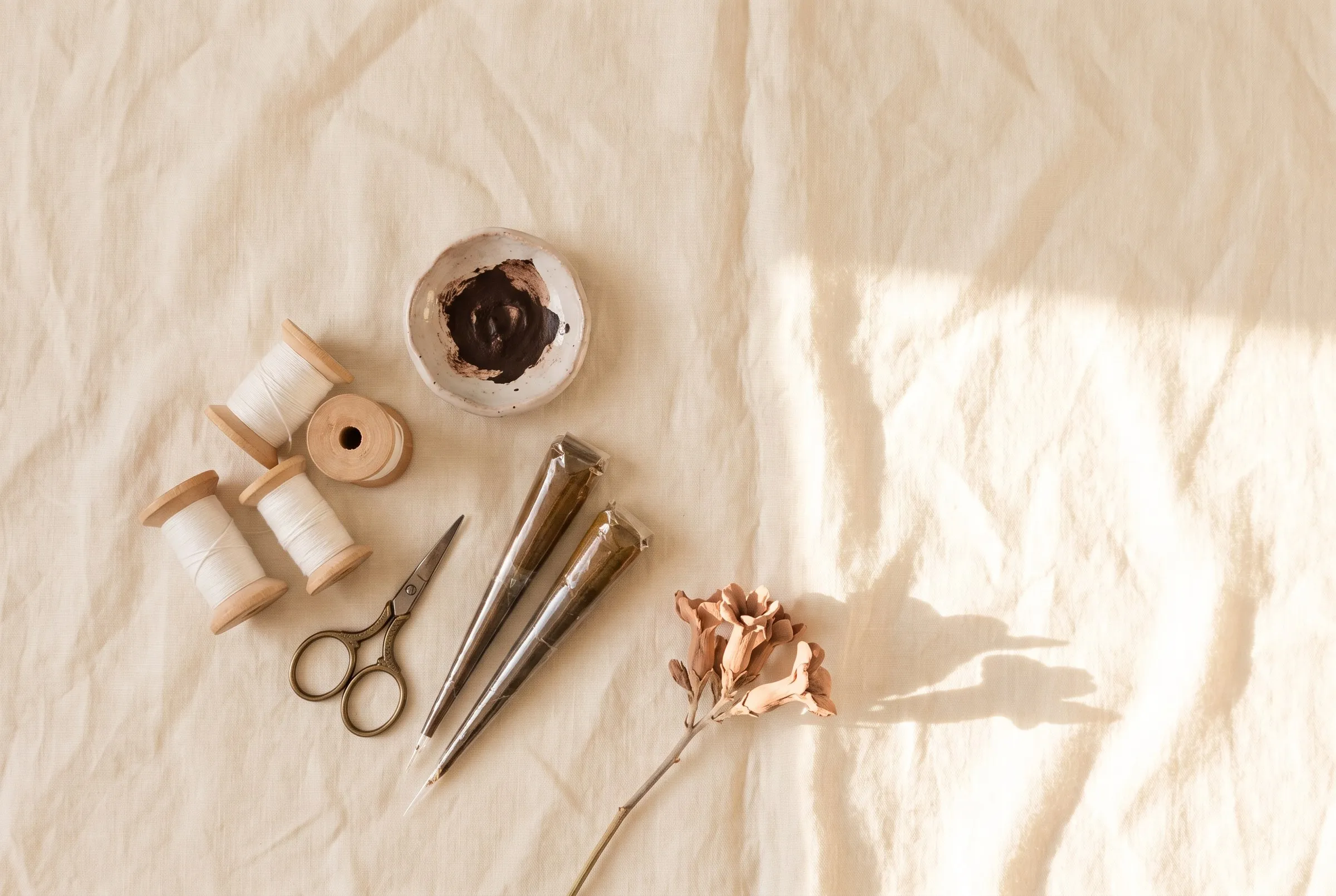 Cotton threading spools, small scissors and henna cones on cream linen