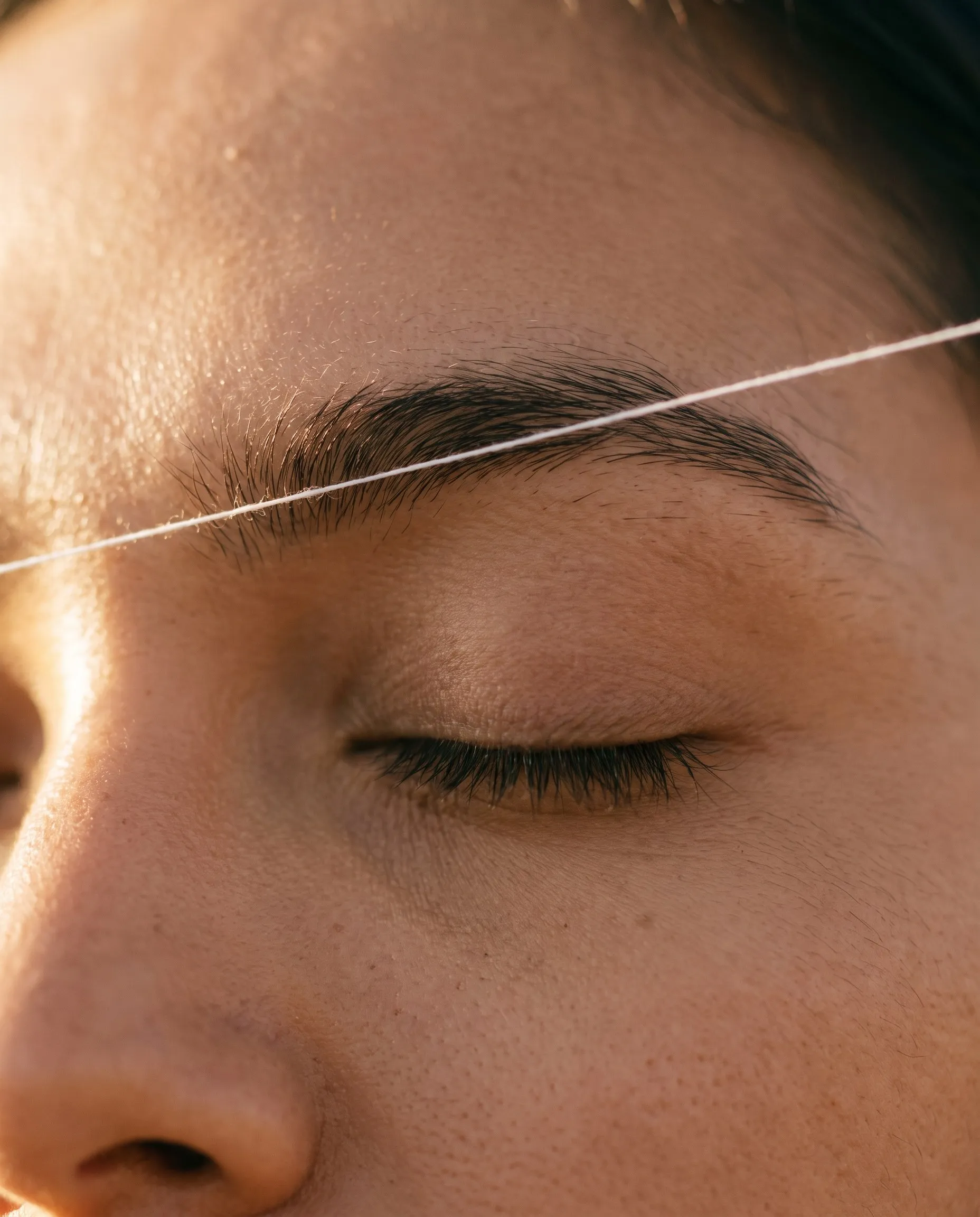Close-up of a closed eye with a cotton thread drawn across the brow line